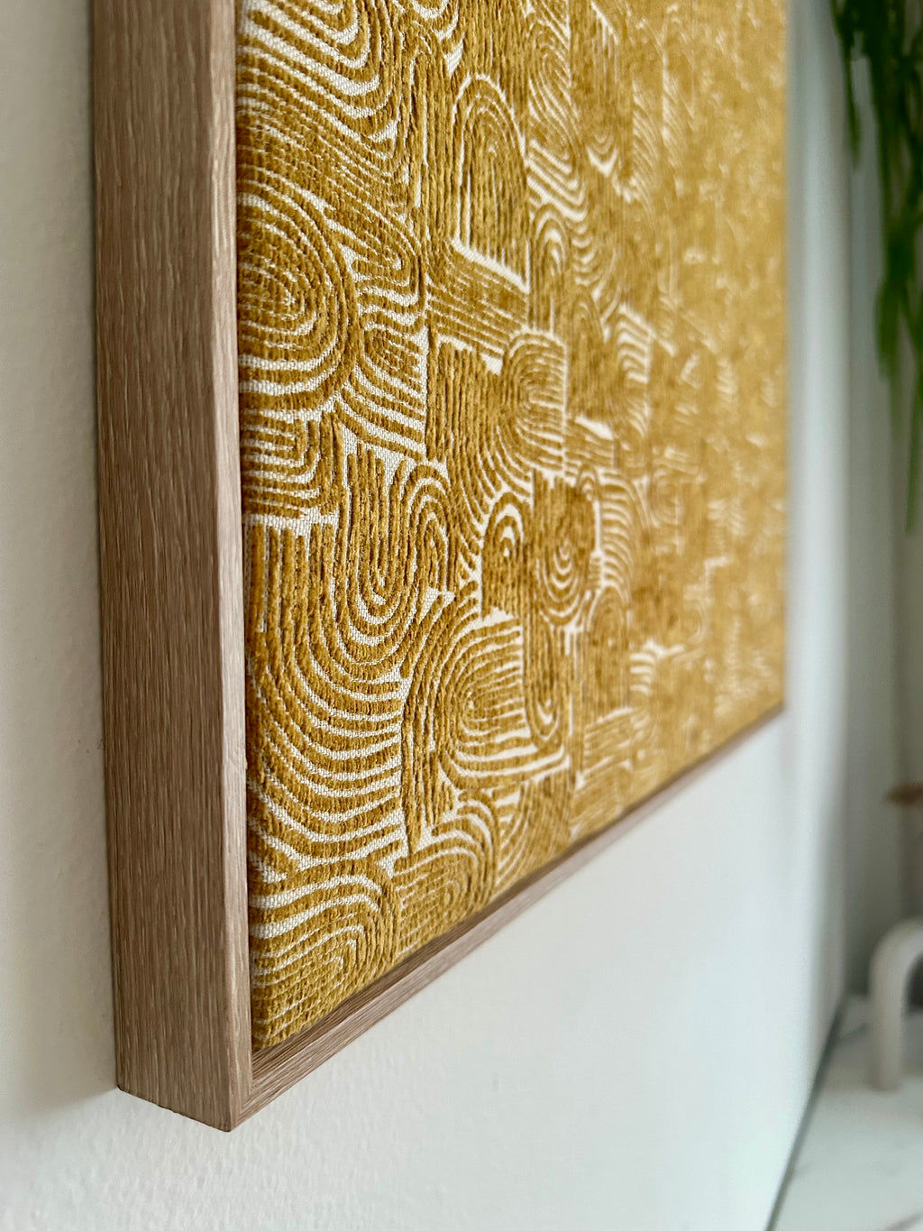 A framed abstract canvas print with a textured gold and cream pattern, mounted on a white wall.