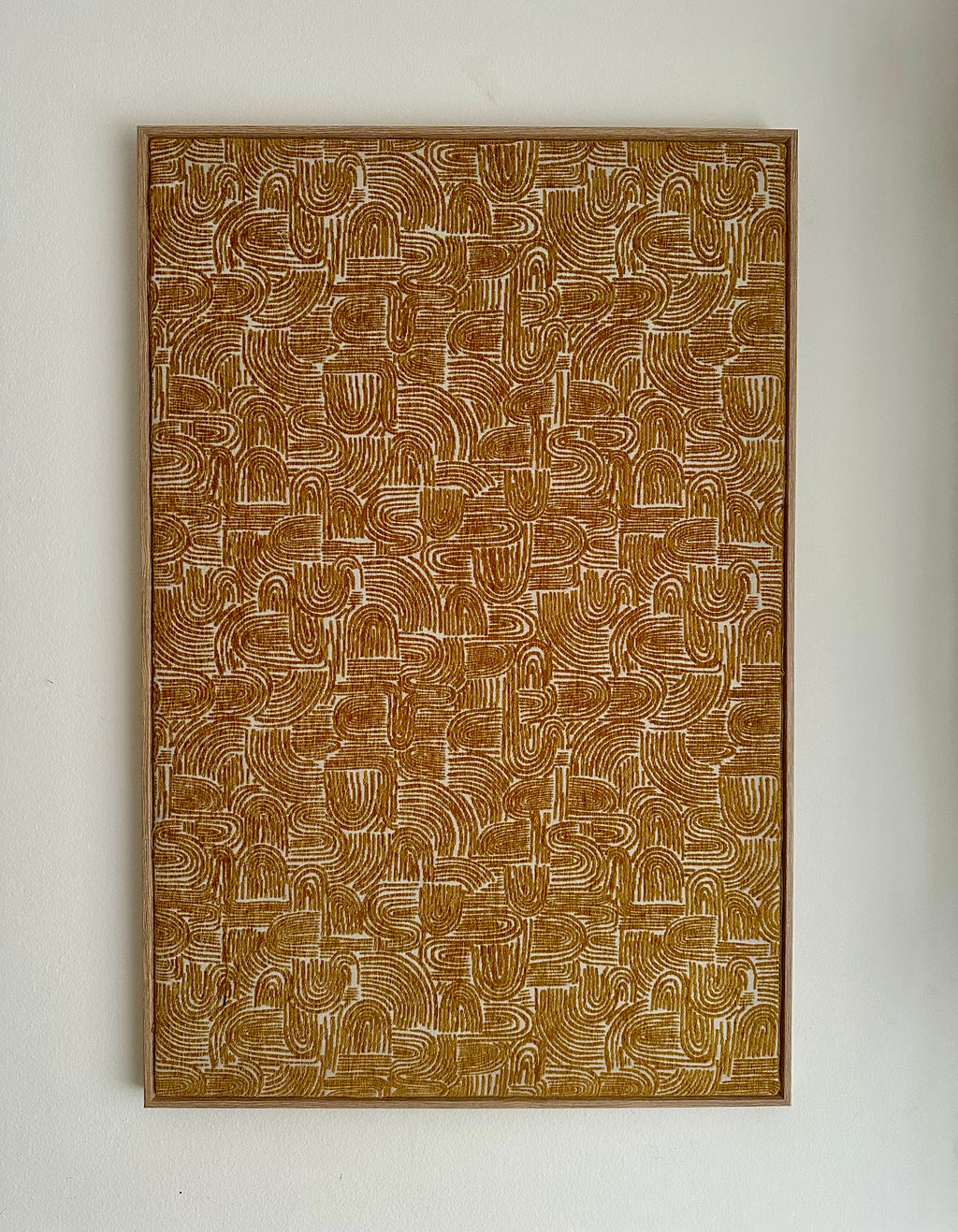 A framed abstract art print featuring a dense pattern of brown and beige wavy, looped lines, mounted on a plain off-white wall.
