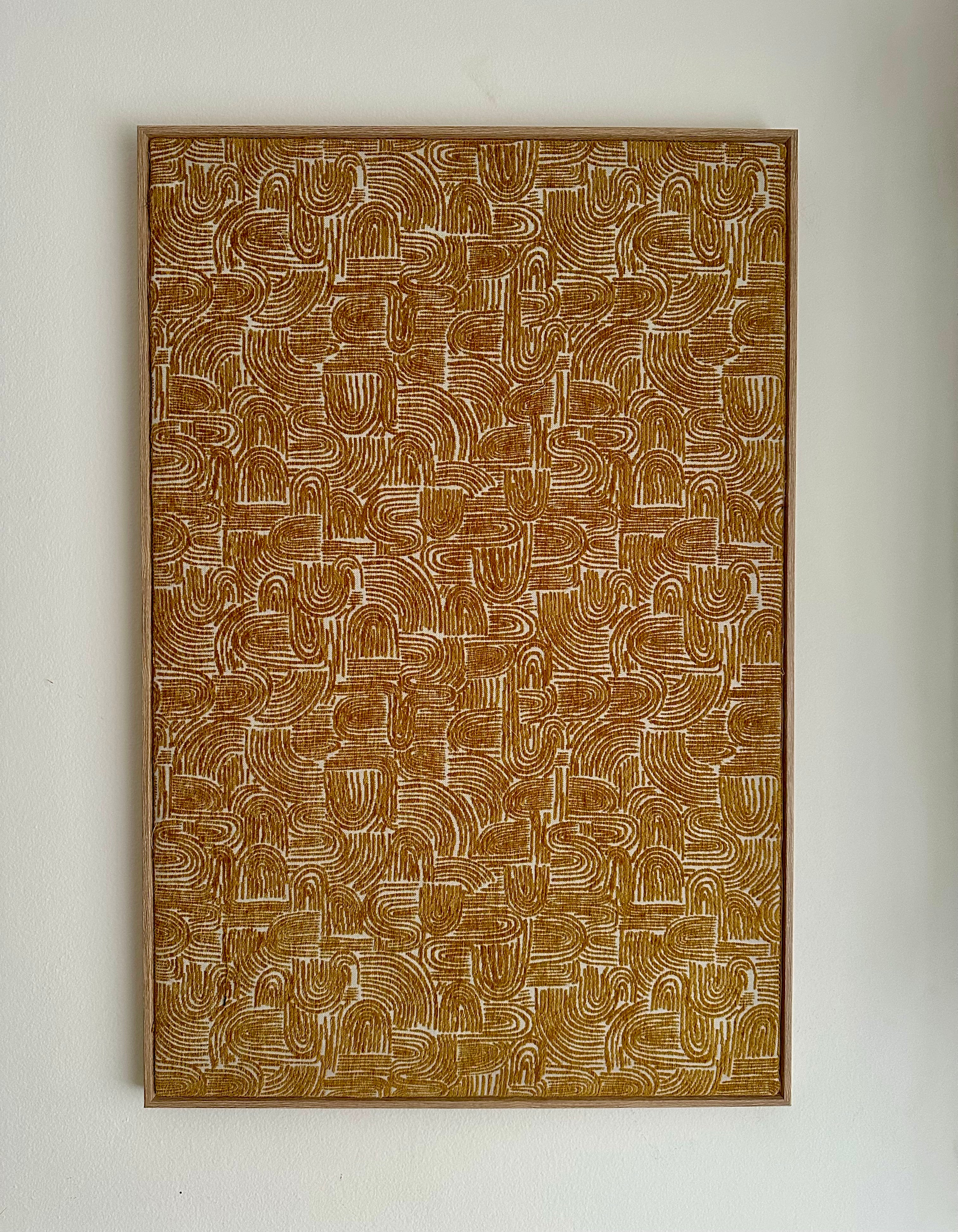 A framed abstract art print featuring a dense pattern of brown and beige wavy, looped lines, mounted on a plain off-white wall.