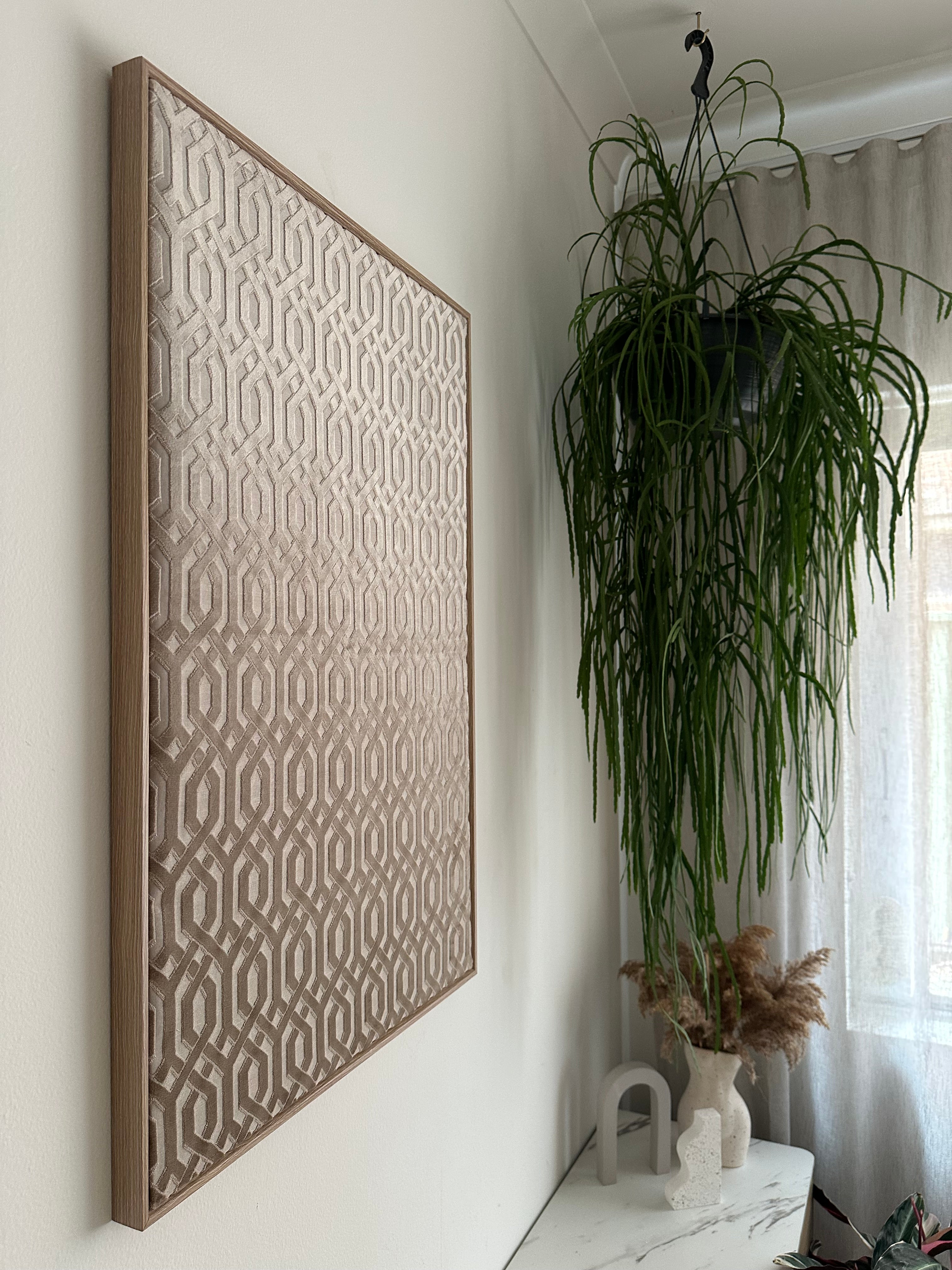 A rectangular decorative tray with a raised geometric pattern, shown on a white tabletop with a potted green plant and dried floral decor in the background.