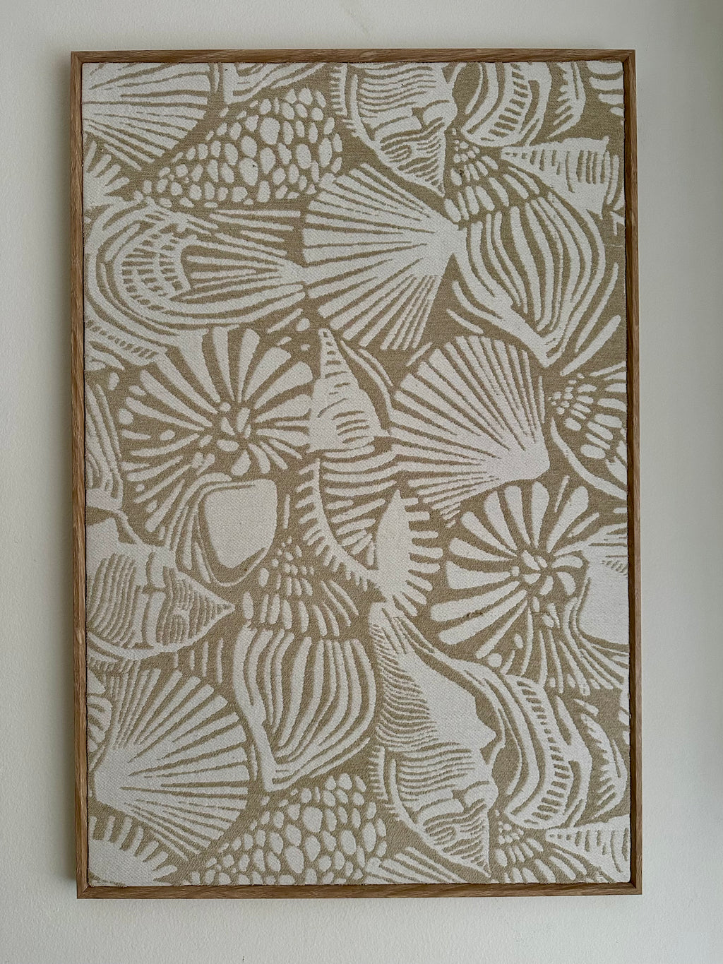 Framed wall art featuring an abstract seashell pattern in beige and off-white tones, mounted on a light neutral wall.