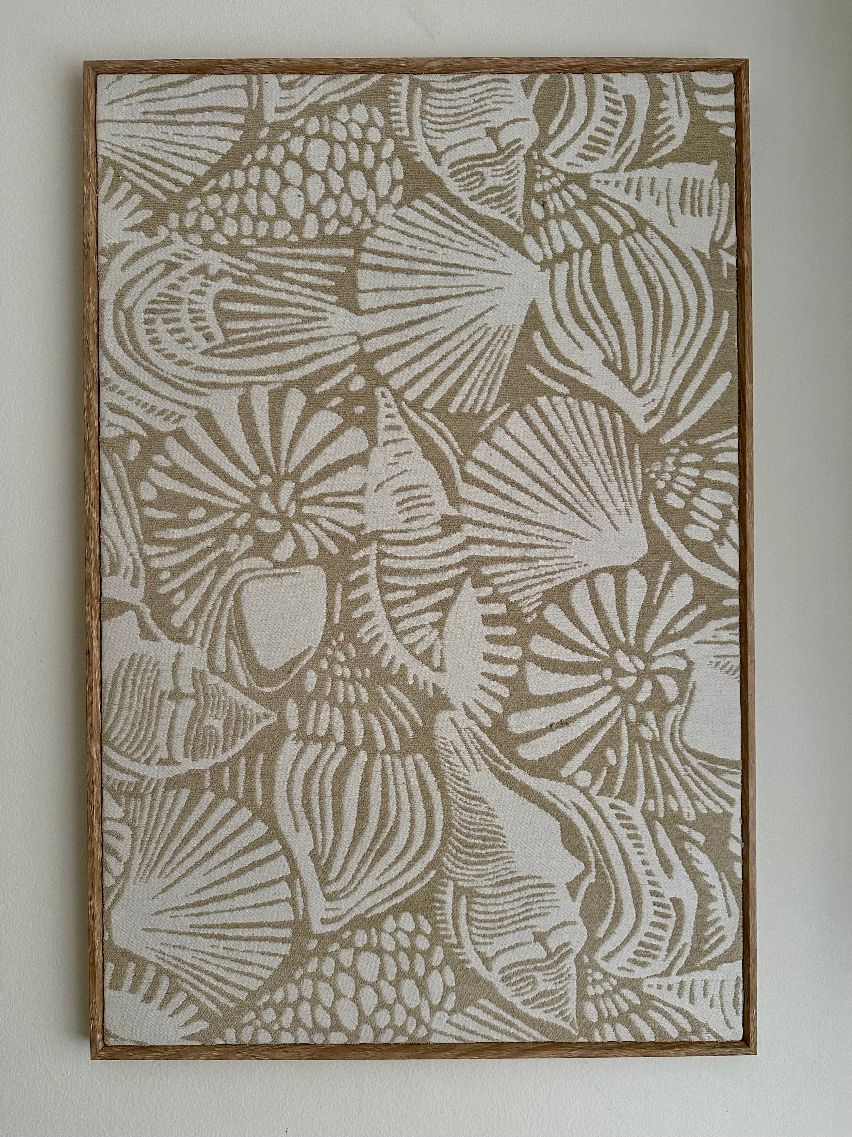 Framed wall art featuring an abstract seashell pattern in beige and off-white tones, mounted on a light neutral wall.