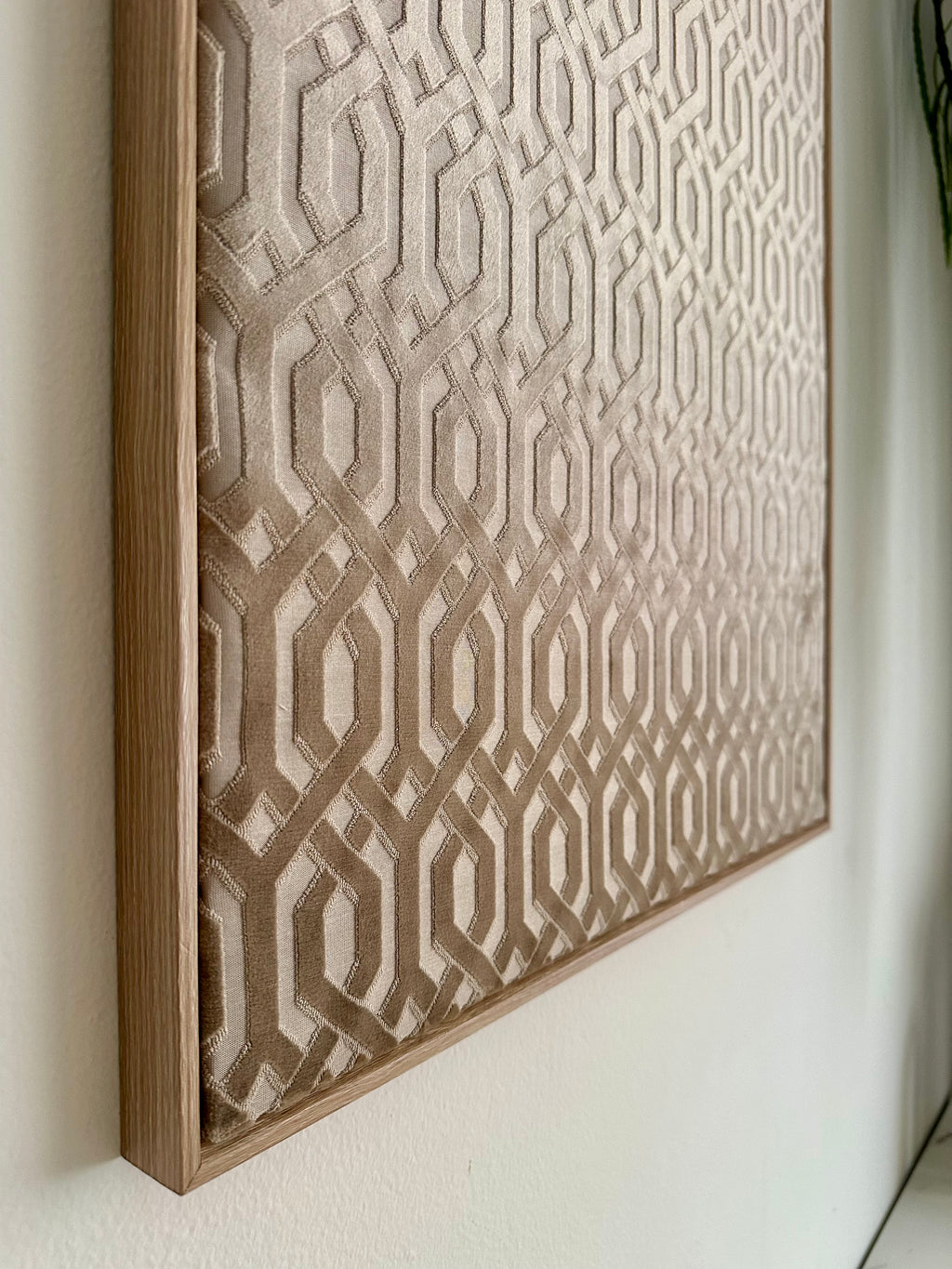 A framed wall art piece with a geometric interlocking pattern in beige and taupe tones, mounted on a white wall.